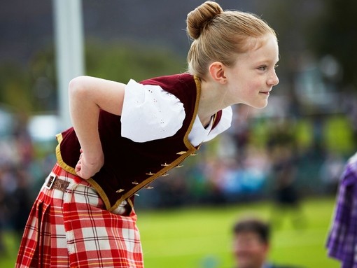 A young girl wearing a kilt leans forward while dancing