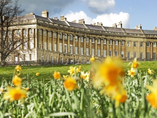 External view of regency style building of the Royal Crescent, Bath through a field of blurred out daffodils in the foreground,