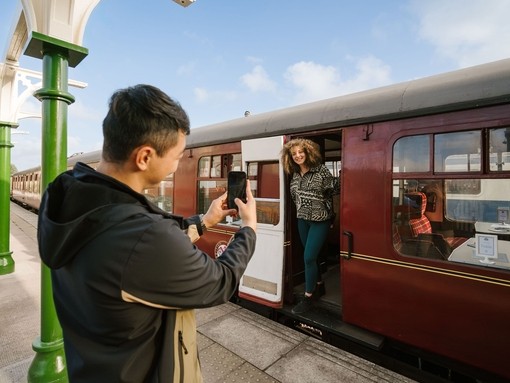 A man taking a picture of a woman standing by the door of a train at a station platform.