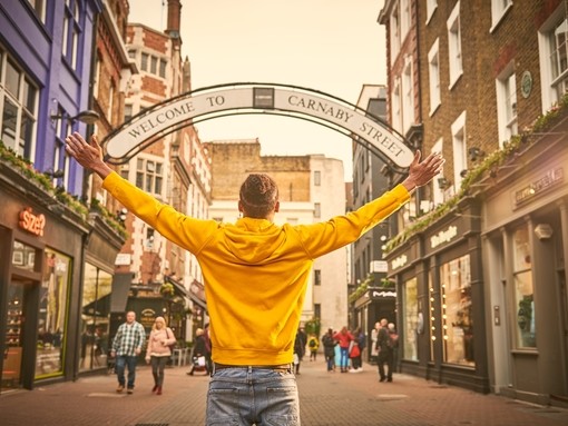 A man posing for the camera in front of a 'Welcome to Carnaby Street' sign in London.