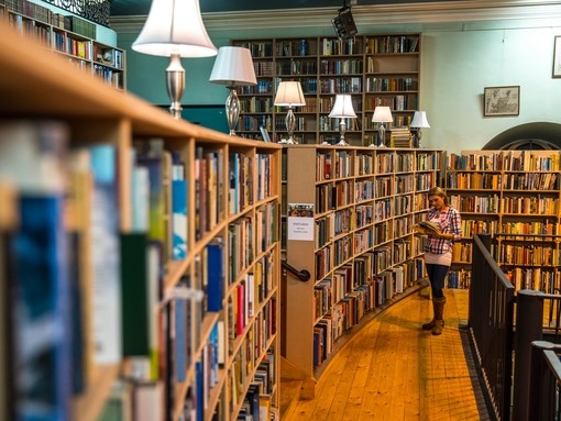 A woman standing by the shelves looking at a boo
