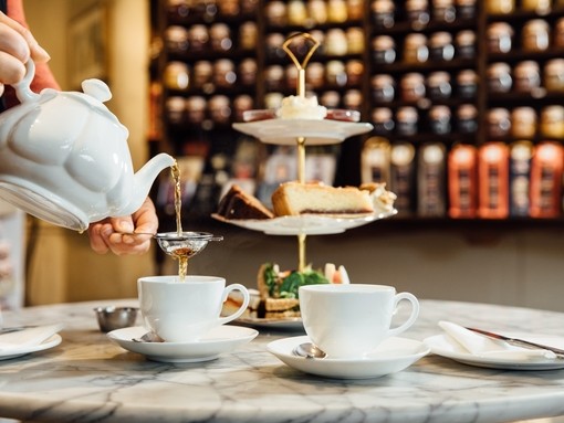 Close up of person pouring cup of tea from white teapot
