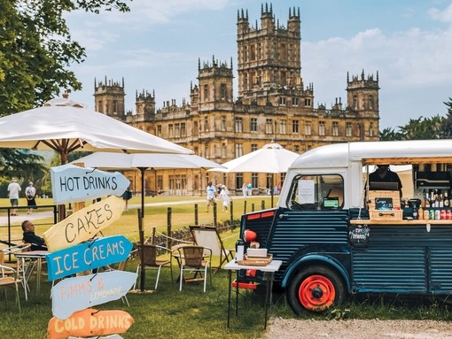 Food truck and direction signs at a festival at Highclere Castle with house behind