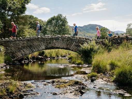 Group of friends out walking in the lakes crossing bridge in the Lake District