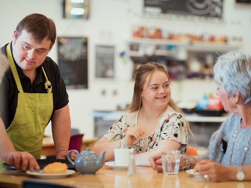 A person with Downs Syndrome serving customers in the cafe