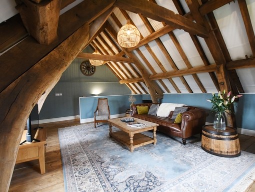 Lounge area at the top of a timber framed building, with exposed ceiling beams, a large leather sofa and wooden coffee table facing a flat-screen TV at Rowley Farm Holidays. Bronze winner of the New Tourism Business of the Year in the VisitEngland Awards for Excellence 2022