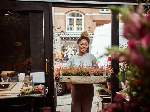Young woman entering her flower shop carrying a tray of heather plants