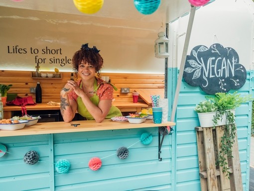 Young mixed race woman stood in the hatch of a food truck smiling, ready to serve