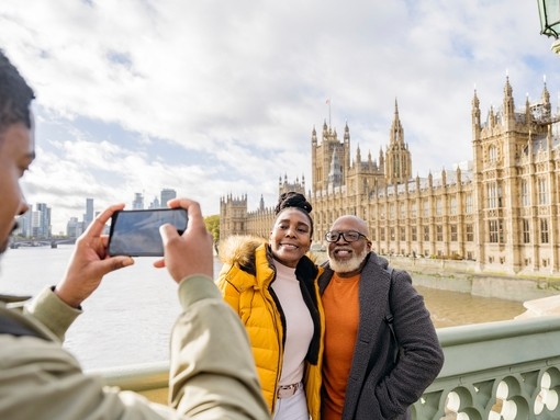 A man photographing mature couple with River Thames and Houses of Parliament in background.