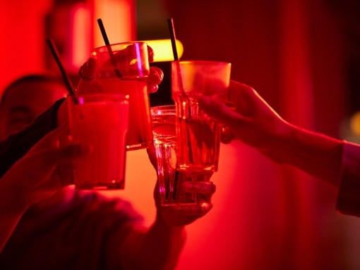 Cropped image of male and female friends toasting drink glasses at bowling alley.