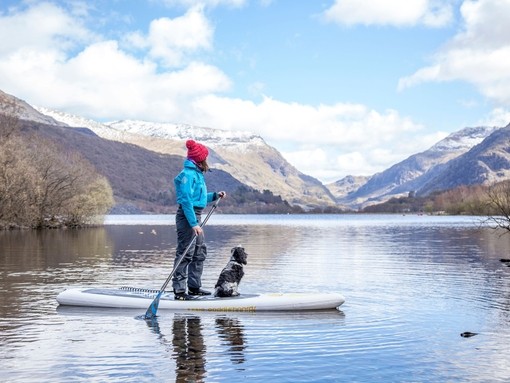 Woman and dog on a paddle-board on lake near mountains