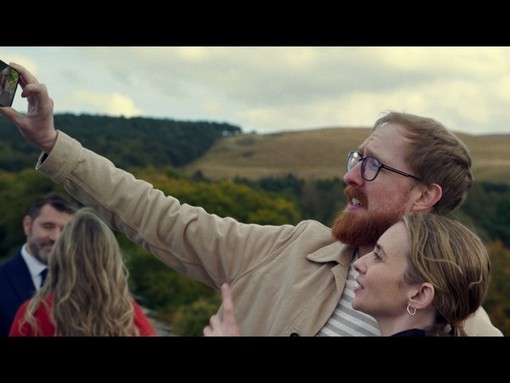A man takes a selfie with a woman in the grounds of a heritage house