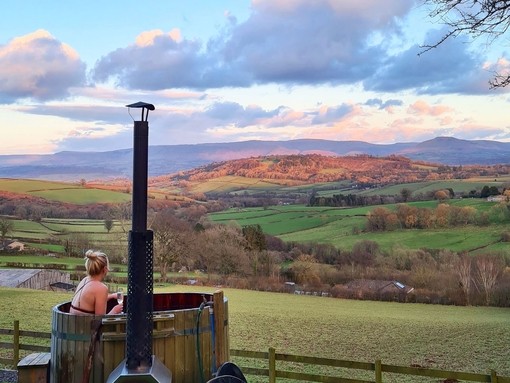 Young woman sitting in a hot tub looking at mountains in the distance holding a glass of champagne, evening light