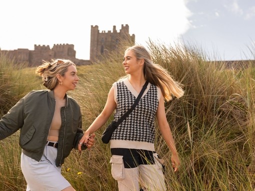 A couple walking in the sand dunes near Bamburgh Castle