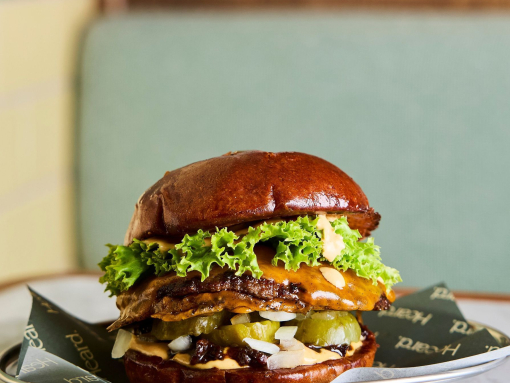 A burger stacked with meat, cheese, pickles and lettuce on a plate, on a marble table.