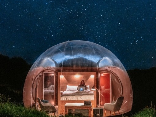 Large glamping bubble pod lit up with woman inside