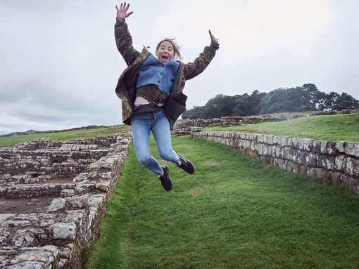 Girl leaping into the air with raised arms near stone wall