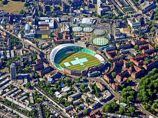 Aerial view scanning over city with large cricket ground, parks and buildings