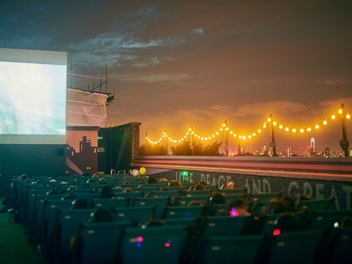 People watching a movie on a large screen at night with the city skyline in the distance