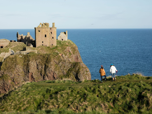 Two women walking along a grassy clifftop, near a castle