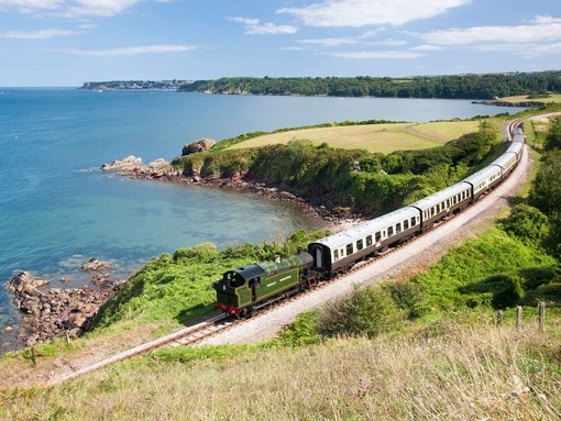 Steam train on railway line along coastline. Sea views