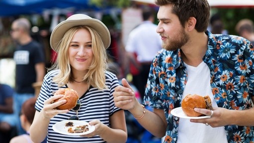 Couple eating burgers at food market.