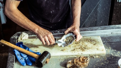 A man (no face shown) prepares an oyster at a seafood market in Whitstable, England
