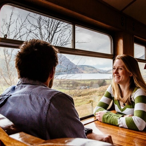 Couple, sat at a table inside train carriage, looking out