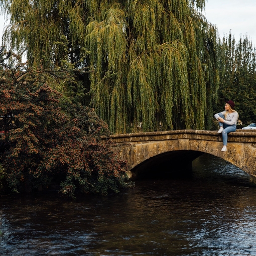 Blond woman wearing hat and jeans sitting on bridge