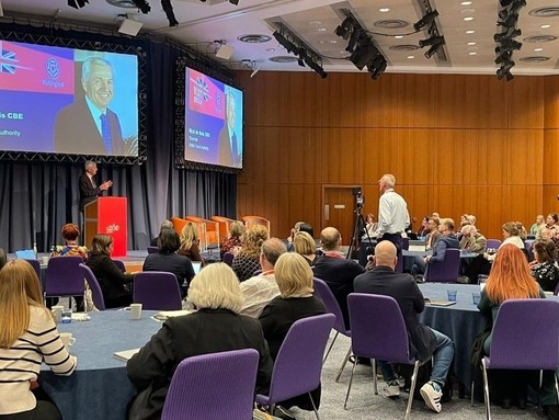 BTA Chairman Nick de Bois CBE stands behind a podium onstage and speaks to a room of 80 delegates at the VisitBritain Business Events Association Conference