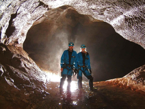 A couple standing in ankle-deep water within a back lit cave