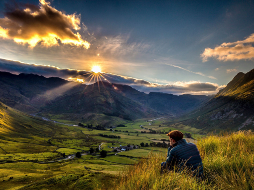 Man sitting in long grass watching sunrise between valleys