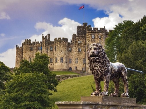 An historic castle with a UK flag at full mast and with a lion statue out the front.