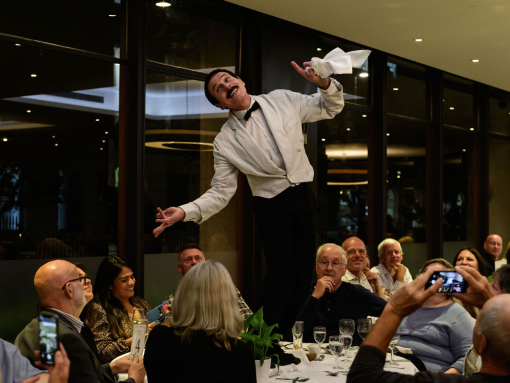 Actors in costume on the set of a farcical play with a waiter parading on a table.