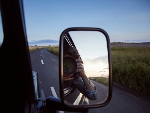 Reflection of man with camera in side view mirror of car