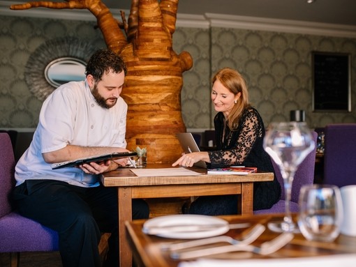 Head Chef and female nutritionalist sat in empty restaurant discussing menu plans for The Green House Hotel, Bournemouth