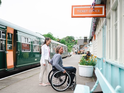 Man using a wheel chair and woman about to go into the ticket office of Grosmont Station