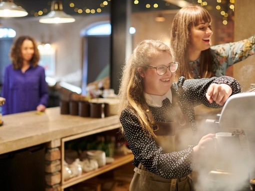 A young woman working the coffee machine with colleague assisting in cafe