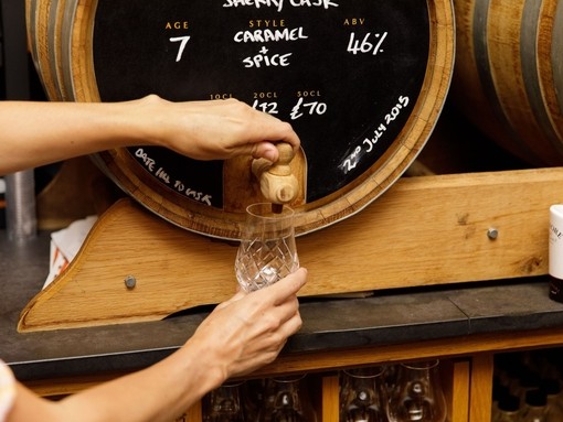Woman's hands pouring a dram of whisky from a barrel.