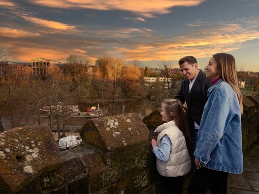 A family of three look out over a town river from a bridge.
