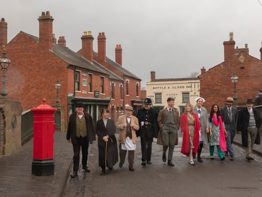 Group of people walking across a bridge in old style clothing