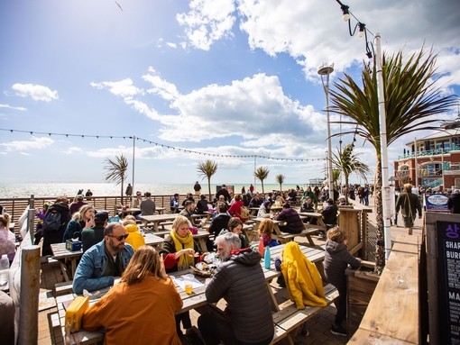 People enjoying drinks and food outside on Brighton sea front at Fortune of War bar in Brighton.