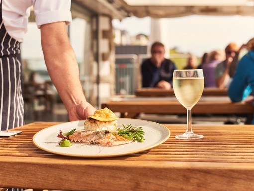 Waiter placing plate of food on table beside glass of wine