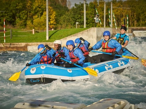 Group of people in a white water raft with paddles on water with rapids