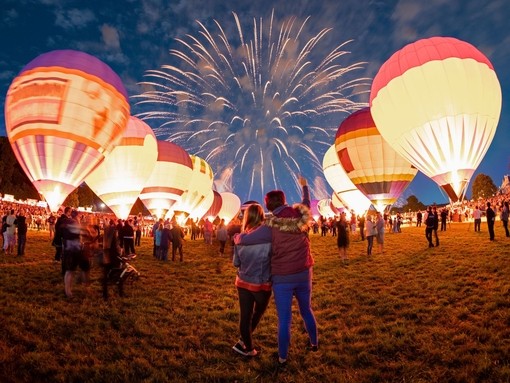 Couple watching grounded hot air balloons and fireworks in the night sky