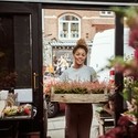 Young woman entering her flower shop carrying a tray of heather plants